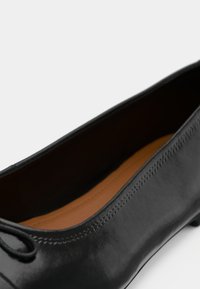 Μαύρο δερμάτινο μπαλαρινάκι με στρογγυλή μύτη, λεία υφή, ελάχιστες λεπτομέρειες ραφής και εσωτερική επένδυση σε ταν απόχρωση.