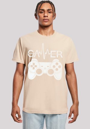 Beige Baumwoll-T-Shirt mit einem weißen Grafikdesign eines Gaming-Controllers und dem Wort "GAMER" darüber. Kurze Ärmel, lockere Passform. Klassisches Design.