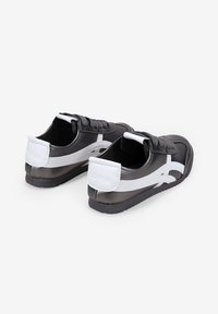 Zapatillas en blanco y negro con una parte superior de cuero suave, diseño con cordones, rayas en contraste y suela de goma texturizada.