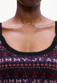 Lilla kootud t-särk mustade ribatud kaelustega, korduva "TOMMY JEAN" mustriga ja väikese logo sildiga punaste, valgete ja siniste aktsentidega.