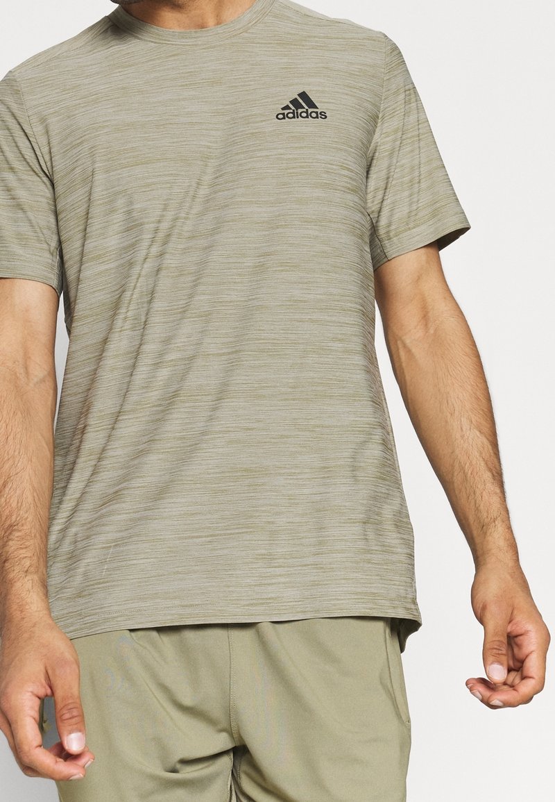 Kurzärmliges, hellolivgrünes Adidas-T-Shirt mit strukturiertem Stoff, Rundhalsausschnitt und schwarzem Logo auf der oberen linken Brust.