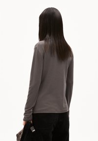Grau langärmliges Hemd aus einem weichen, glatten Material; schlichtes Design mit abgerundetem Saum; getragen mit dunklen Cordhose.