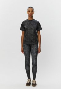 T-shirt s čiernym leopardím vzorom a zodpovedajúce legíny, obe vyrobené z hladkej, elastickej látky. Ľahký dizajn s voľným strihom. Hnedé topánky.