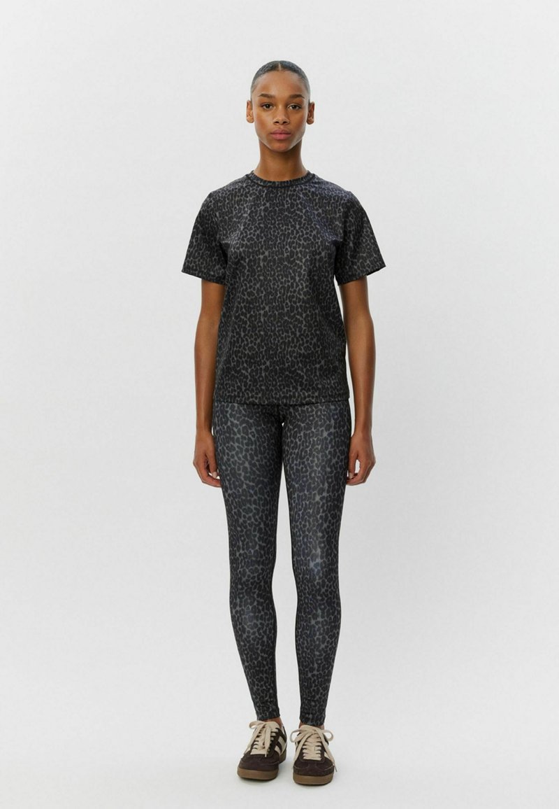 T-shirt s čiernym leopardím vzorom a zodpovedajúce legíny, obe vyrobené z hladkej, elastickej látky. Ľahký dizajn s voľným strihom. Hnedé topánky.
