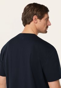 Marineblauwe katoenen t-shirt met korte mouwen, met een klassieke ronde halslijn en minimale stikseldetails op de achterkant.