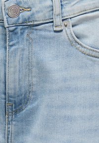 Világoskék farmernadrág, látható elülső zsebbel, fémből készült gombbal és kontrasztos sárga varrással, sima textúrával.