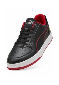 Sneakers in pelle nera con accenti rossi, punta tonda, linguetta testurizzata e logo. Presentano una suola intermedia bianca e perforazioni sulla punta.