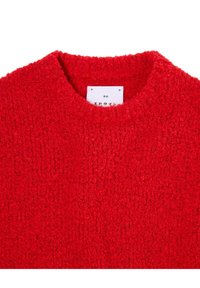 Λαμπερό κόκκινο υφασμάτινο πουλόβερ με υφή, με στρογγυλή λαιμόκοψη και λευκή ετ�ικέτα ρούχων με ιαπωνικό κείμενο μέσα στο κολάρο.