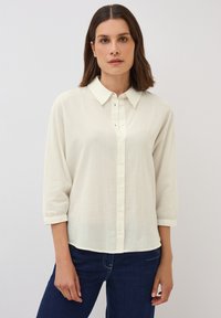 Krémová, lehká blůza s jemnou žebrovanou texturou, tříčtvrtečními rukávy a límečkovým výstřihem. Design s zapínáním na knoflíky.