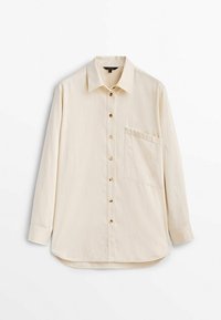 Camicia beige chiaro con maniche lunghe, chiusura frontale con bottoni e una tasca sul petto. Realizzata in tessuto morbido, con bottoni marroni e orlo curvo.