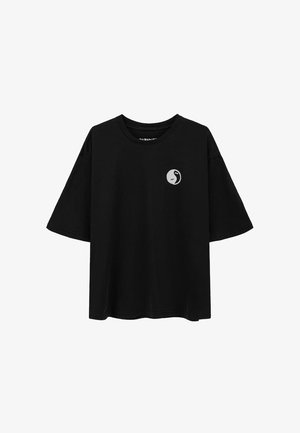 Czarna koszulka z krótkim rękawem o luźnym kroju, z okrągłym dekoltem i małym białym logo po lewej stronie klatki piersiowej. Gładka tekstura.