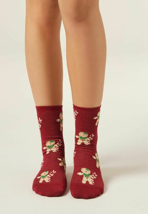 Czerwone skarpetki do kostek z motywem piernika, zielonymi akcentami i lizakami, wykonane z miękkiego materiału o gładkiej fakturze.