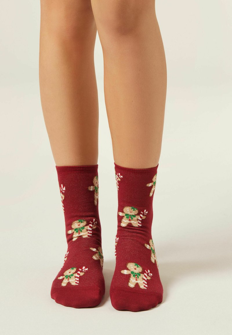 Calzini alla caviglia rossi con motivo di pan di zenzero, dettagli verdi e bastoncini di zucchero, realizzati in materiale morbido con una texture liscia.