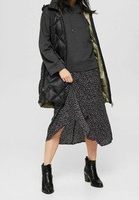 Černá prošívaná vesta přes šedou mikinu s kapucí, ve spojení s černou midi sukní s puntíky a černými kotníkovými botami na podpatku, vystihující různé textury.