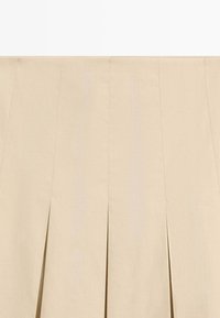 Beige plisseret nederdel med høj talje og strukturerede lodrette syninger, lavet af tykt stof.