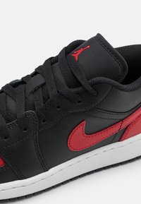 Musta nahkainen lenkkari, jossa punaiset yksityiskohdat, näkyvä Nike-logo, mustat nauhat ja kuvioitu ulkopohja. Minimalistiset suunnitteluelementit.