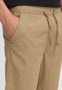 Beige bomullsbukser med elastisk midje og snor, med sidelommer og en myk, strukturert fabric finish.