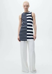 Top a righe senza maniche in blu navy e bianco, caratterizzato da una combinazione di righe larghe e strette, abbinato a pantaloni bianchi a gamba larga.