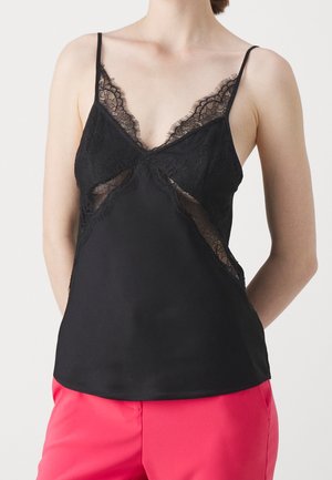 Schwarzes Camisole mit Spitzenakzenten, V-Ausschnitt, dünnen Trägern und einer weichen Textur. Kombiniert mit hellrosa Hosen.