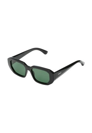 Lunettes de soleil rectangulaires noires avec montures épaisses et verres vert foncé, vue en angle montrant une branche avec le logo Komono.