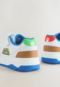 Weiße Sneakers mit blauen Akzenten, einem braunen Ziegelmuster, "Super Mario"-Logo sowie grünen "L"- und roten "M"-Details an der Ferse.