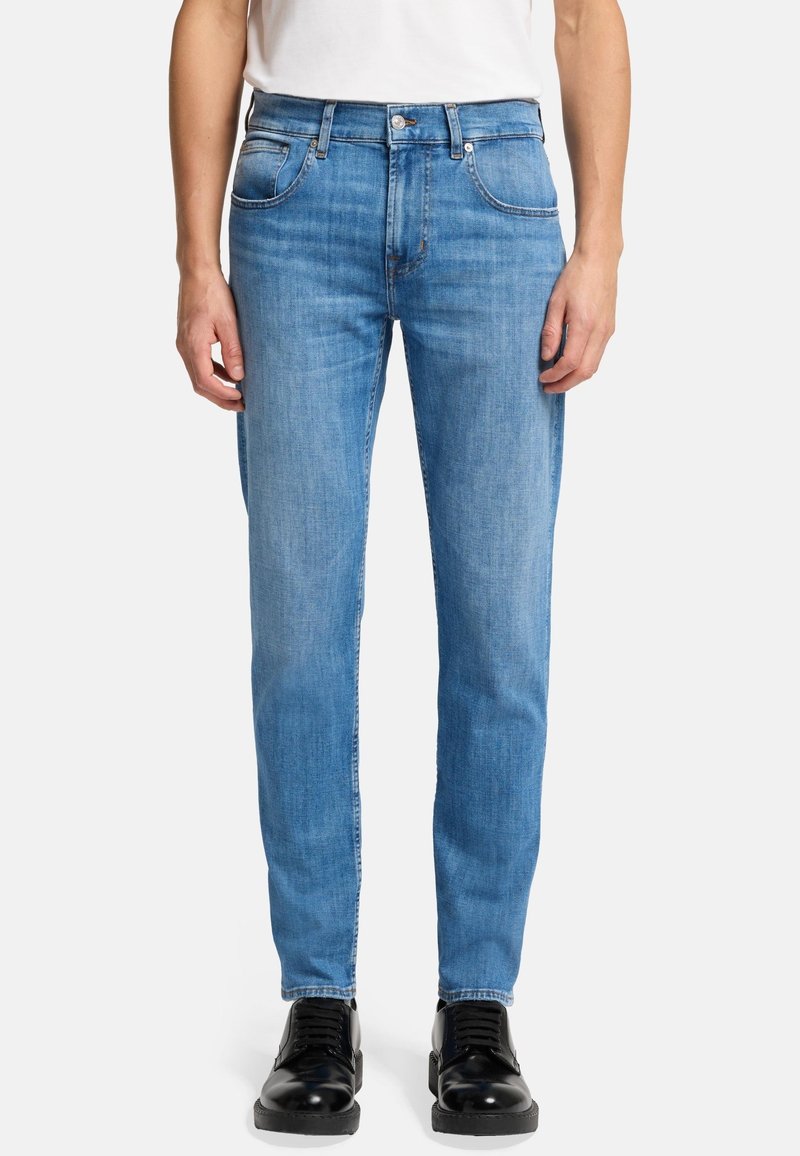 Hellblaue Jeans aus Denim mit geradem Bein, fünf Taschen und subtilen Steppdetails, getragen mit schwarzen Schnürschuhen.