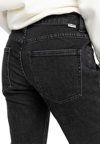 Black denim jeans featuring a fitted design, back pockets, and a Billabong brand label on the waistband. Textured with a slight fade.