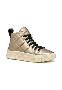 Zapatilla alta con parte superior acolchada de color dorado metálico, cordones negros, suela de goma beige y un tirador en el talón para poner y quitar fácilmente.