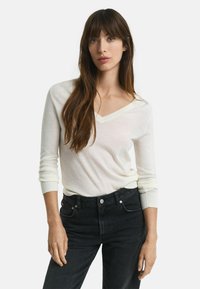 Pull à col en V, à manches longues, fabriqué en tissu doux de couleur crème, associé à un jean en denim noir taille haute avec poches avant et une fermeture à boutons.