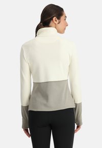 Leichter, zweifarbiger Pullover mit hohem Kragen; oben in Creme und unten in Dunkelgrau. Hat lange Ärmel und eine weiche Textur.
