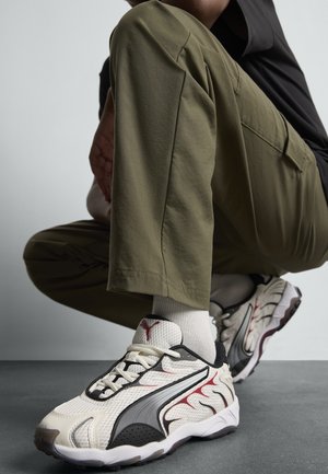 Sneakers met een witte mesh bovenkant, zwarte accenten en rode details; gemarmerde zool, lichtgewicht ontwerp en traditioneel vetersysteem.