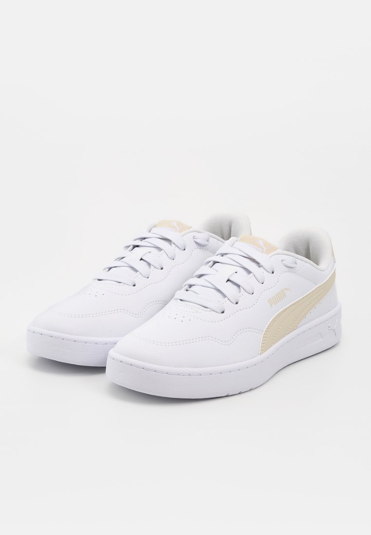 Baskets basses blanches Puma avec bande logo beige et lacets, présentées côte à côte sur un fond blanc uni.