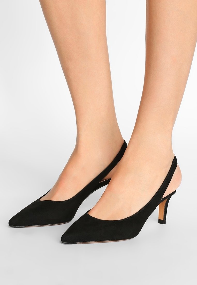 Escarpins slingback en suède noir avec un bout pointu, un talon fin et un design ajouré sur les côtés. Texture lisse avec une finition minimaliste.