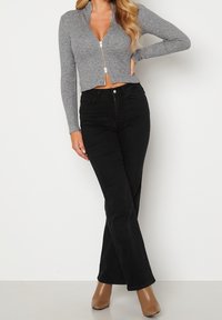 Gray ribbed zip-up crop top with long sleeves, paired with high-waisted black flared jeans, and tan heeled ankle boots.