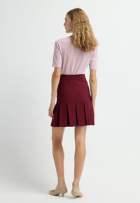Burgundy plisserad kjol med en åtsittande midja, tillsammans med en ljusrosa kortärmad topp. Modell i beige klackar. Enkel, ren design.
