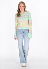 Maglione a righe pastello, lavorato a maglia, con maniche lunghe e collo rotondo, abbinato a jeans a gamba larga blu chiaro e sneakers bianche. La texture appare morbida.