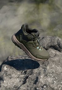 Olive-green hiking shoe with textured mesh upper, padded collar, and flexible rubber sole. Features a secure lacing system and branding accents.