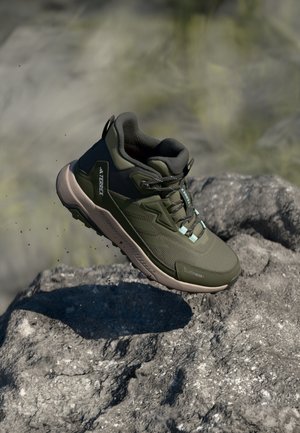 Chaussure de randonnée vert olive avec un dessus en maille texturée, un col rembourré et une semelle en caoutchouc flexible. Elle dispose d'un système de laçage sécurisé et d'accents de marque.
