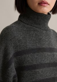 Dunkelgrauer Rollkragenpullover aus weichem Strickmaterial, mit horizontalen schwarzen Streifen über den Stoff. Nahaufnahme zeigt die Textur.
