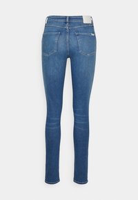 Vaqueros ajustados de mezclilla azul con una textura suave, cintura media, dos bolsillos traseros y un detalle de costura mínimo.