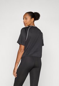T-shirt de sport noir à manches courtes, avec des passepoils blancs le long des épaules et du dos. Tissu léger et respirant.