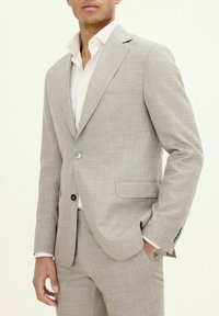 Completo grigio chiaro con finitura testurizzata, chiusura a un bottone, rever a pattina e taschino sul petto, abbinato a una camicia bianca.