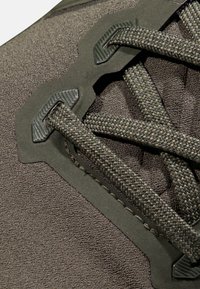 Mörkgrå sportskor i närbild, med texturerad yta, vävda snören och robusta svarta detaljer för säker fäste.