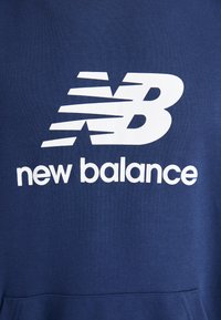 Navy kék pamut keverék pulóver, amelyen egy nagy fehér "NB" logó és a "new balance" felirat található karakteres sans-serif betűtípussal.