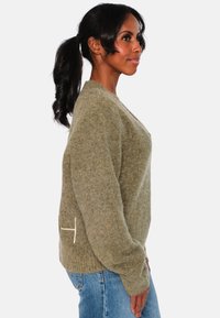 Olivgrön ulltröja med avslappnad passform, ribbade manschetter och en unik vit accent på sidan. Mjuk textur, rund halsringning.