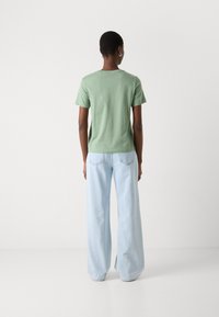 T-shirt verde in cotone con maniche corte, abbinato a jeans a gamba larga di un blu chiaro. Entrambi i capi presentano un design informale e una texture morbida.