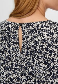 Marineblaues und weißes Blumenmusterkleid mit einer Schlüsselrücken-Design und einem einzigen schwarzen Knopfverschluss sowie strukturiertem Stoff.