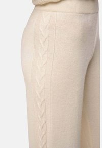 Gros plan sur un pantalon en tricot crème avec un motif de câble tressé vertical sur le côté et une taille côtelée.