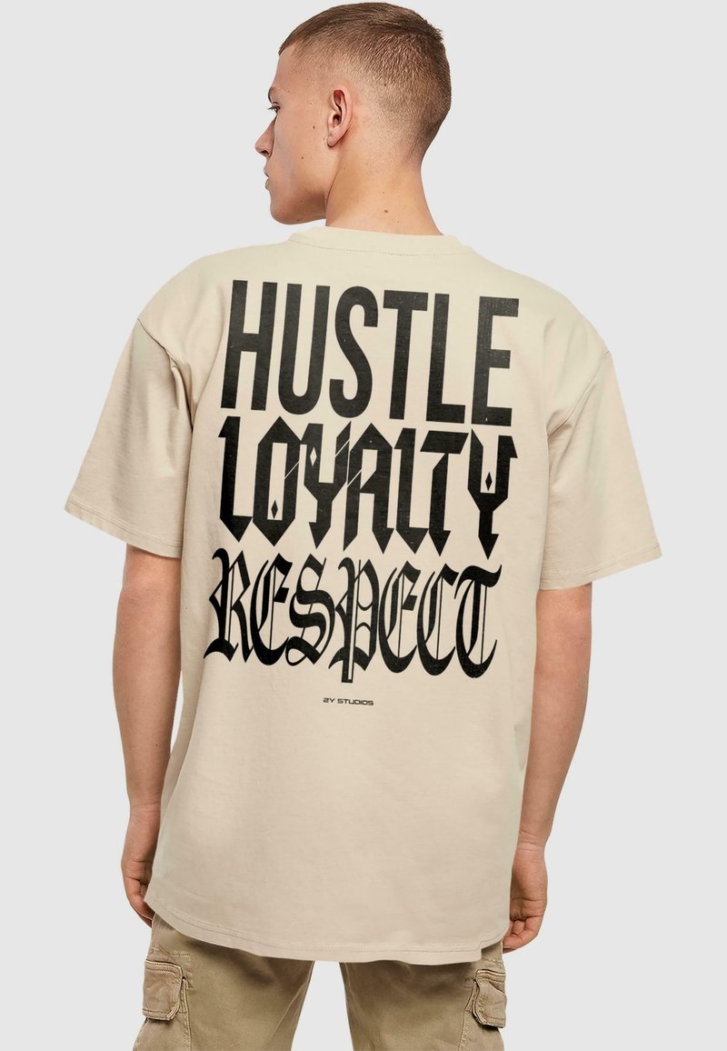 Beige kokvilnas t-krekls ar lieliem melniem gotiskajiem burtiem uz aizmugures: "HUSTLE LOYALTY RESPECT," ar brīvu piegriezumu un īsām piedurknēm.