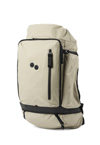 Beige Rucksack mit strukturiertem Oberflächendesign, schwarzen Akzenten, mehreren Fächern und einem großen Haupt-Reißverschlussfach. Verfügt über zwei runde Logos.